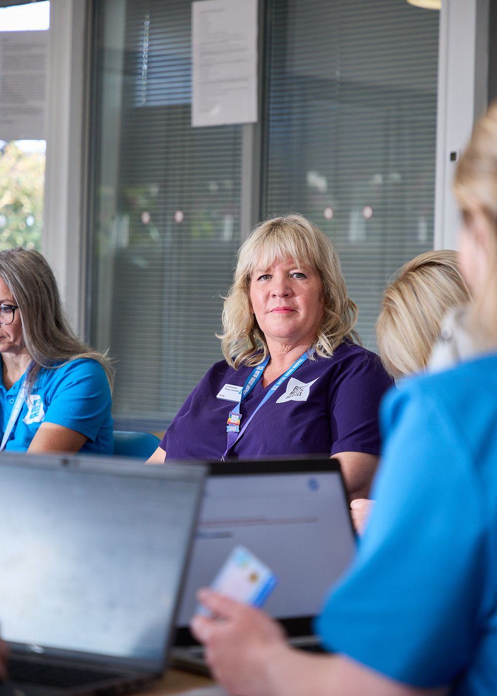 Healthcare professionals in scrubs attending a meeting with laptops in a bright conference room.