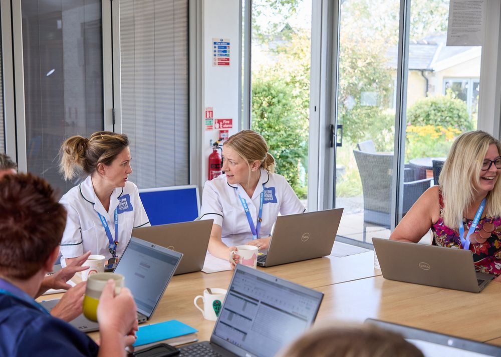 Healthcare professionals in white uniforms working on laptops during a medical team meeting in a bright conference room.