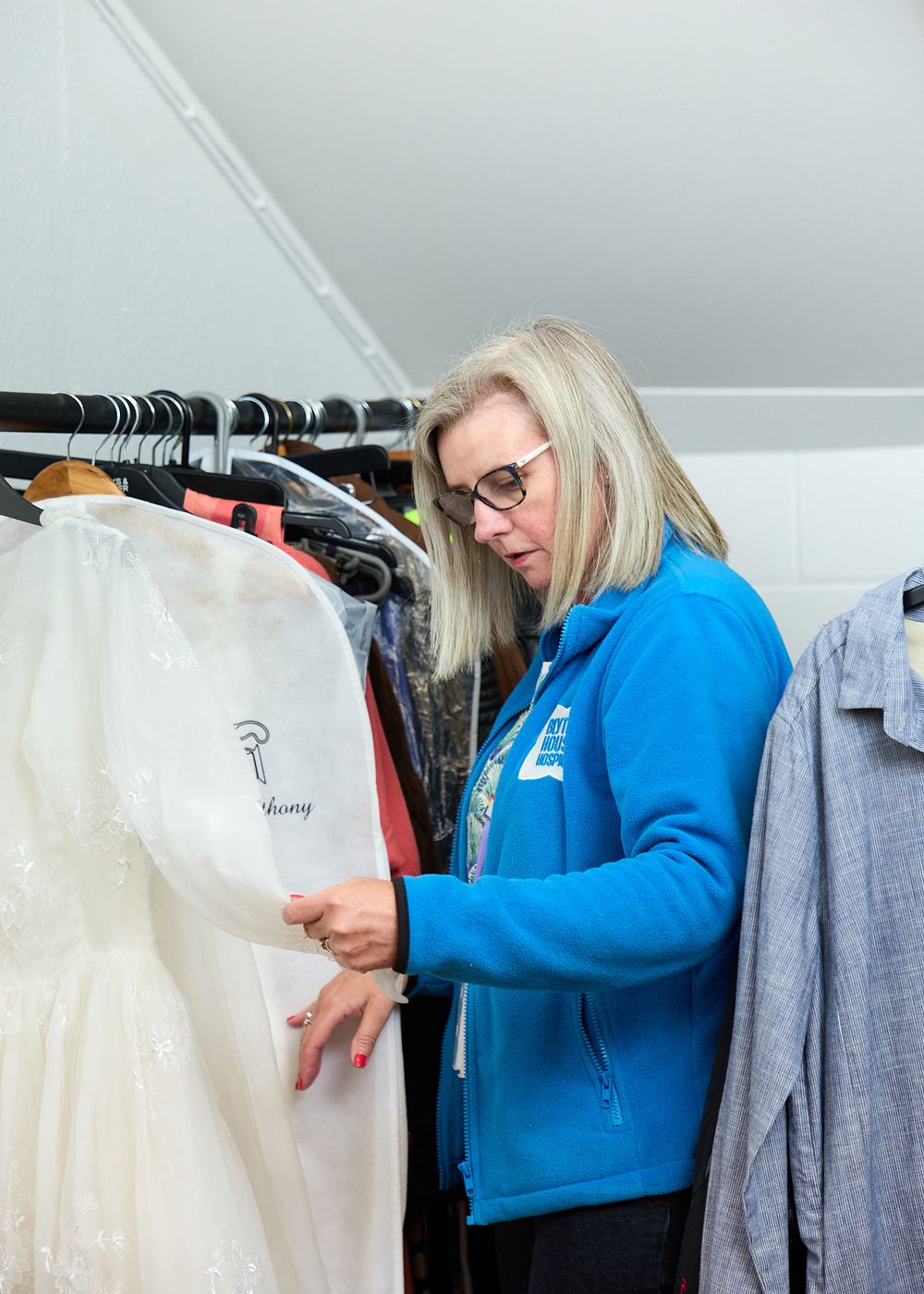 Woman in blue jacket browsing wedding dresses on a clothing rack in a bridal shop.