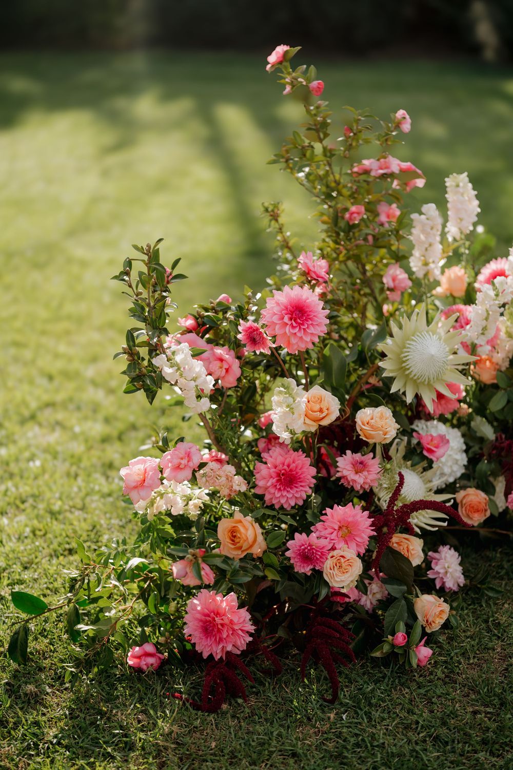 Lush pink dahlia and rose floral arrangement on green grass at an outdoor wedding ceremony.