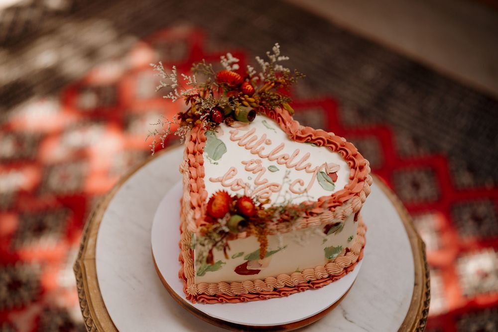 Heart-shaped wedding cake with pink piping, floral topping, and elegant script on a gold charger plate.