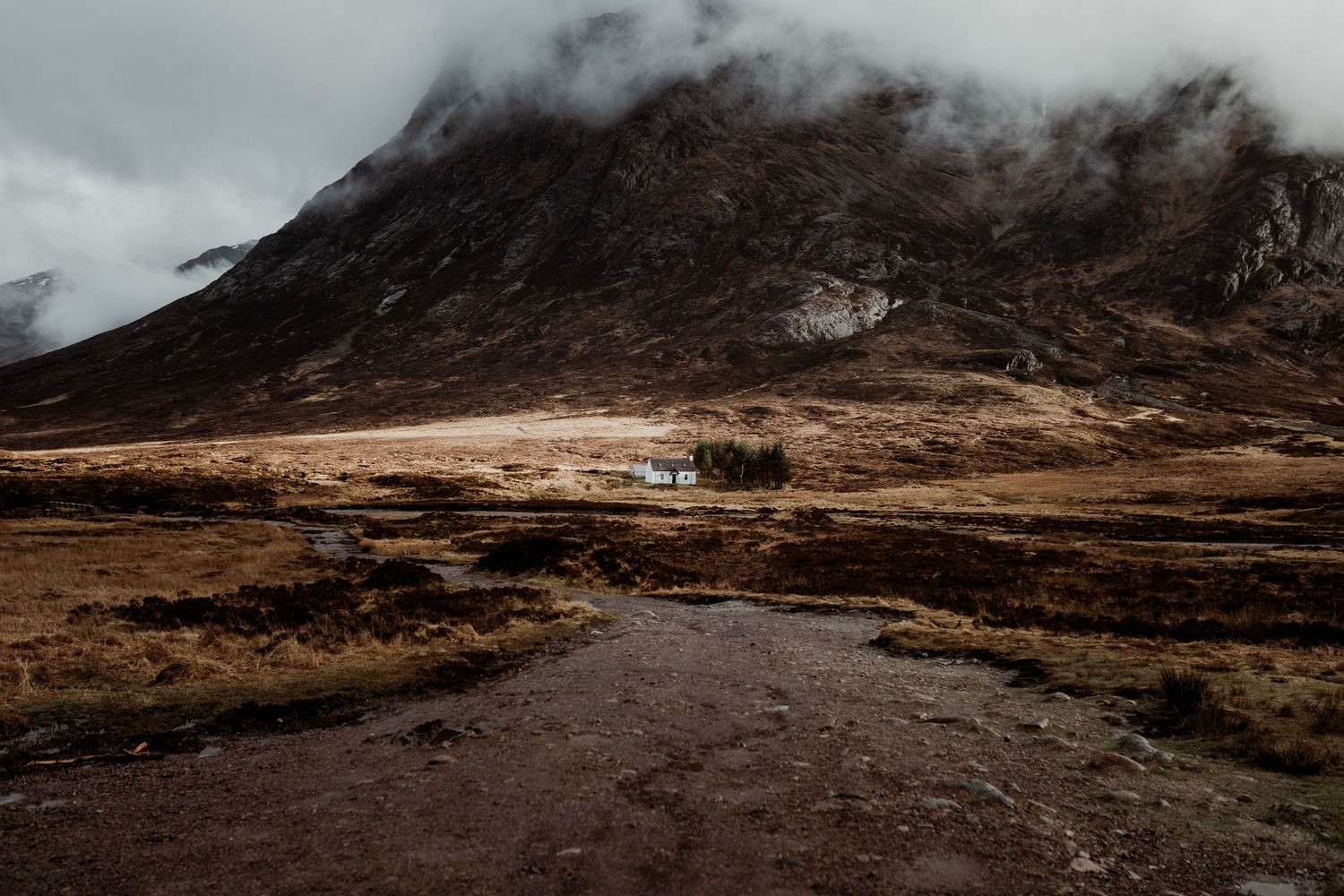 A misty Scottish Highland valley with a white cottage nestled among autumn hills and cascading waterfalls.