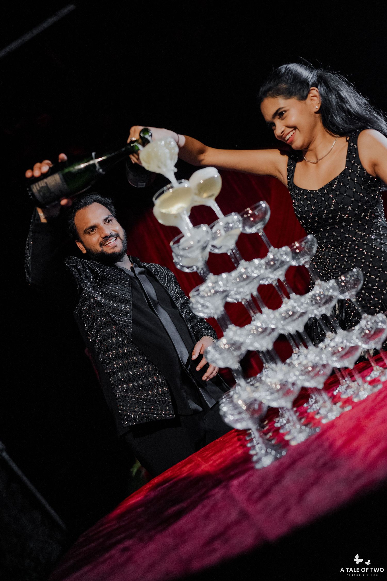 Couple pouring champagne over a glass tower at a glamorous celebration event.