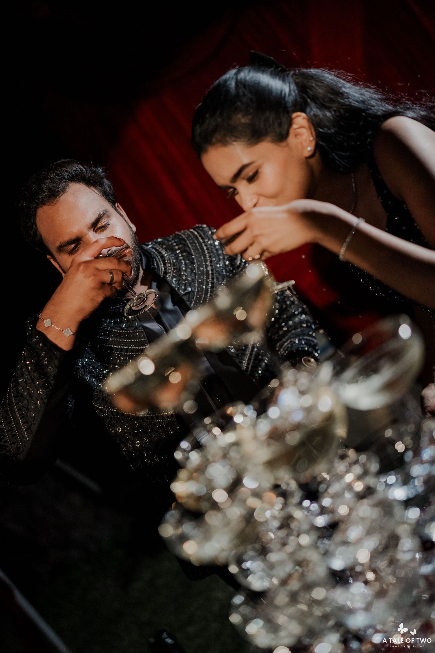 Couple sharing a romantic moment at a glittering wedding reception, dressed in elegant black embroidered outfits.