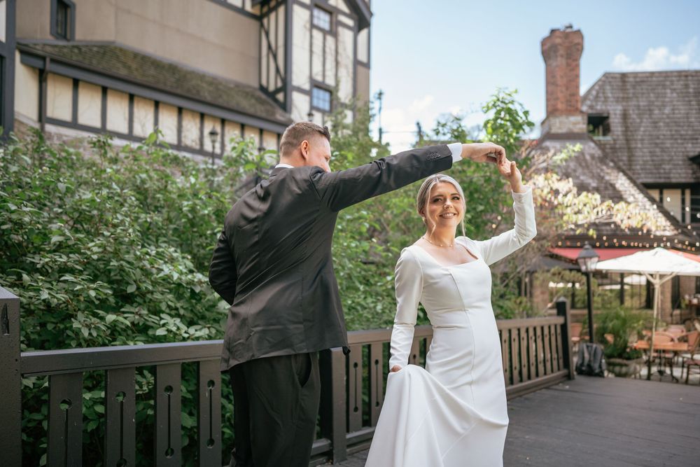 Bride and groom dancing outdoors at wedding venue, bride in elegant white gown smiling as groom twirls her.