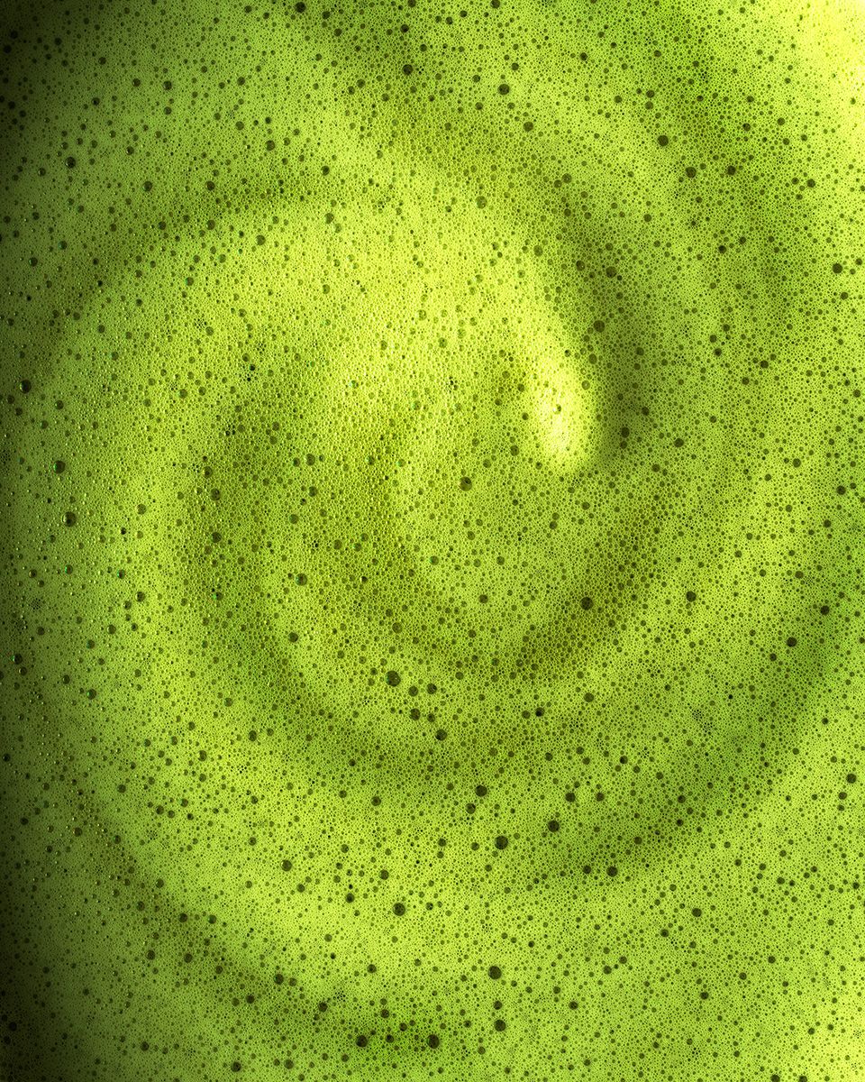 Close-up of vibrant green matcha latte with frothy bubbles forming a swirling spiral pattern on the surface.