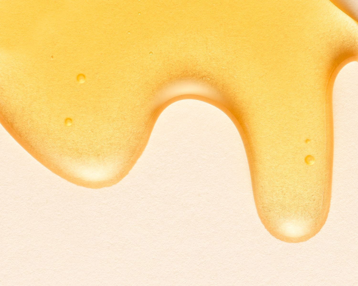 Close-up of golden honey dripping down a smooth surface, showcasing its rich amber color and glossy texture.