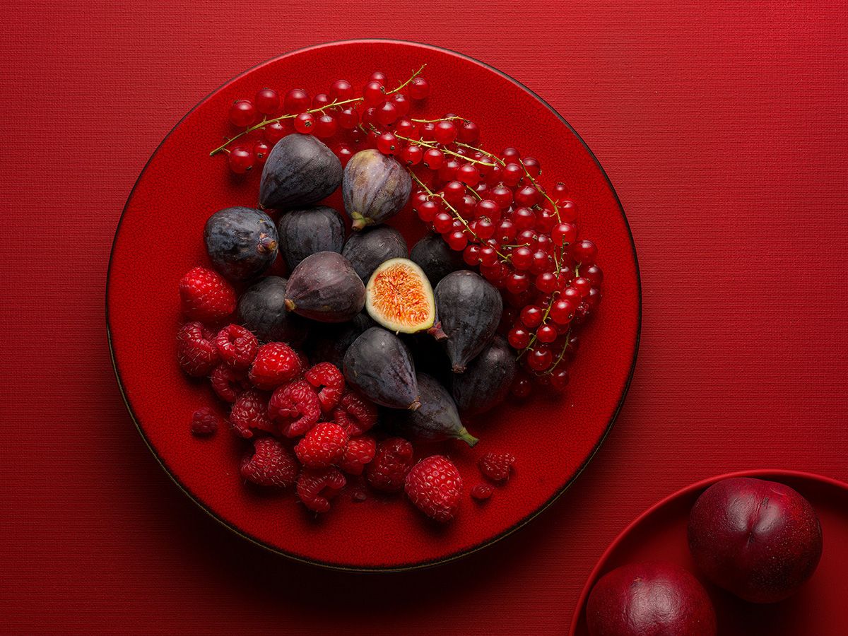 Red plate with fresh figs, raspberries, and red currants on a red background.