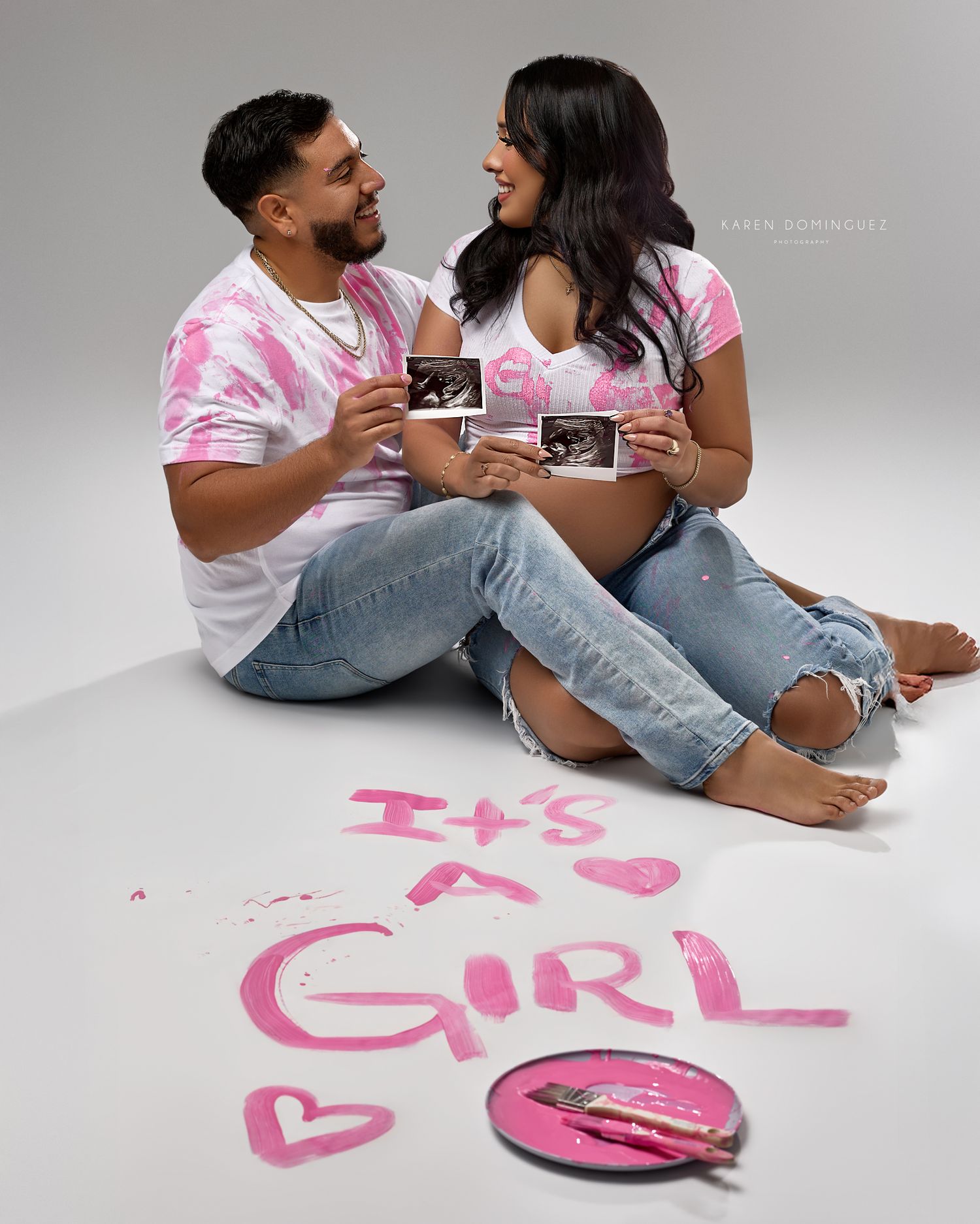 A couple in matching pink shirts and jeans lay on the floor next to pink text written on white paper.