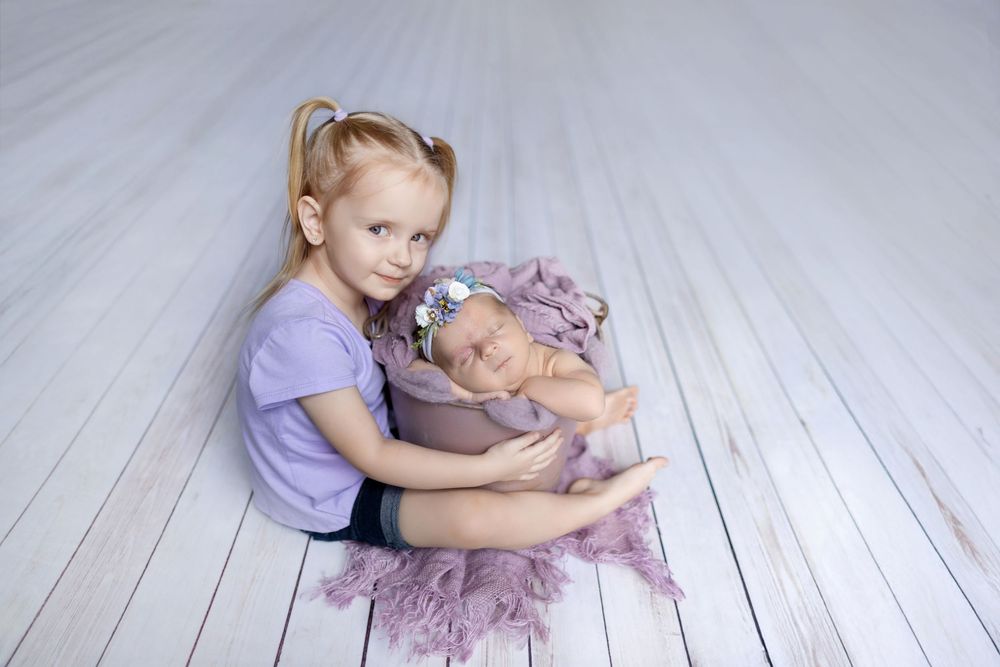 A child in a purple tutu dress sits on a white wooden floor holding a gray plush bunny toy.