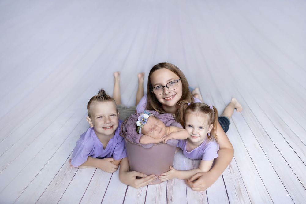 A series of family portraits on a white wooden floor with subjects wearing coordinating purple and gray outfits.