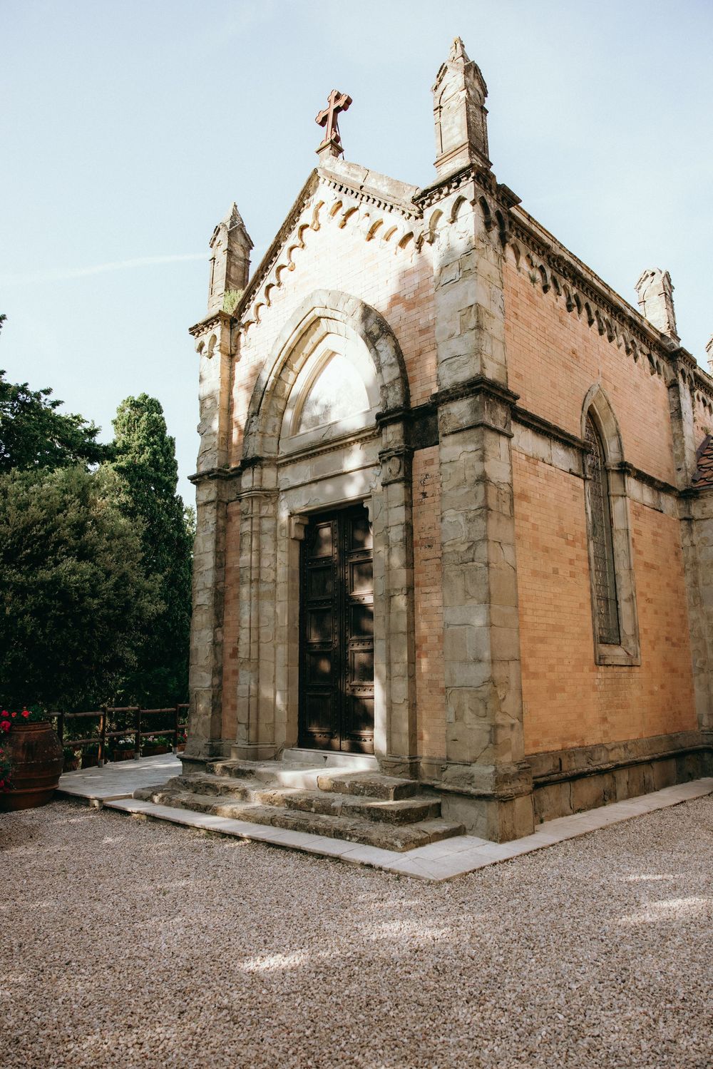 Historic stone chapel with Gothic arches and crosses stands in a gravel courtyard.