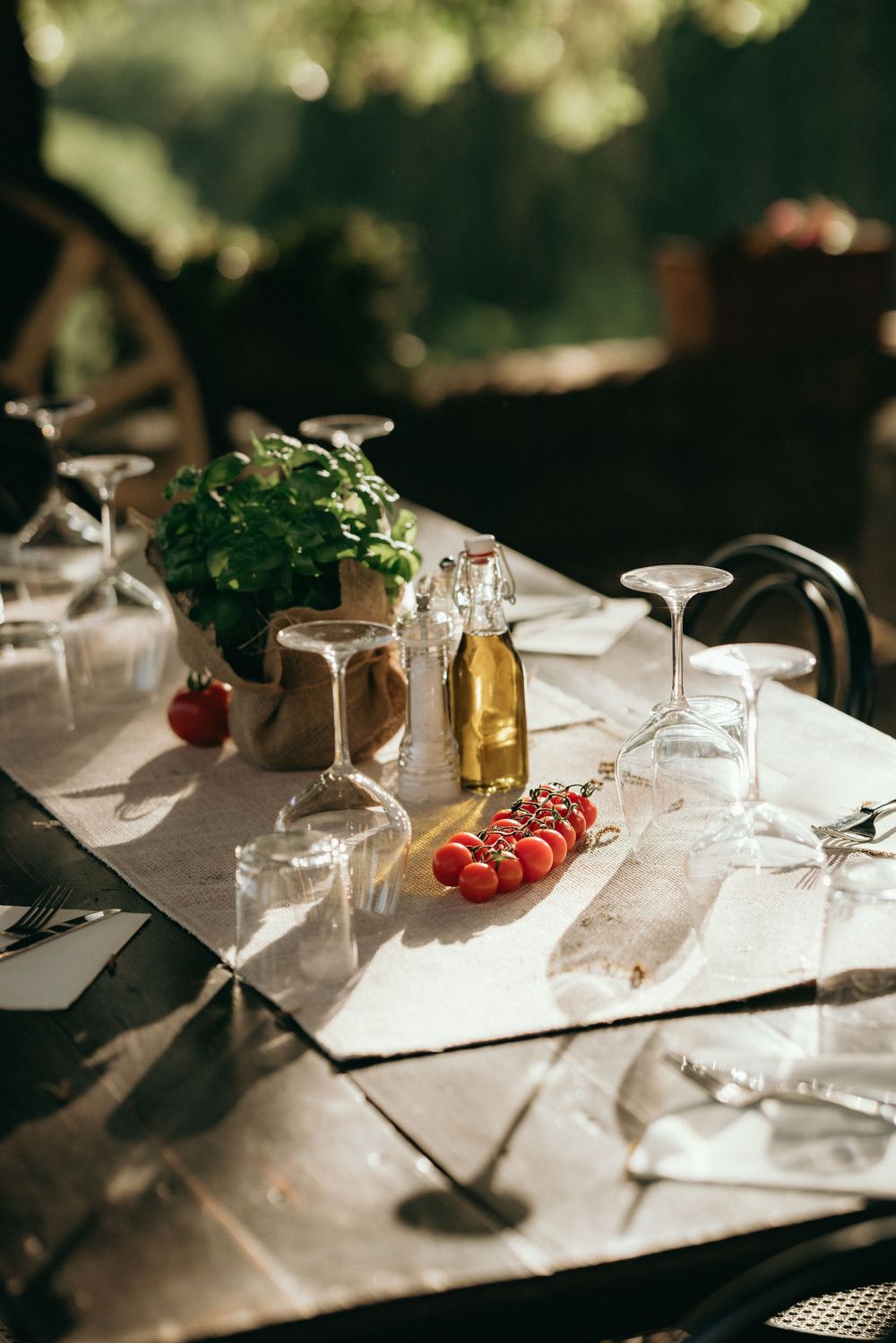 Elegant table settings with wine glasses and fresh tomatoes in natural sunlight.