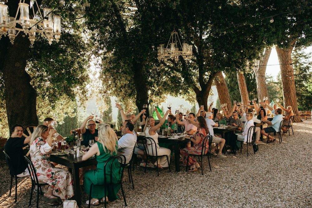 Outdoor garden reception with guests seated at tables under tree canopy.