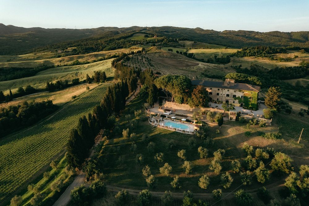 Panoramic view of rolling Tuscan hills with villas and swimming pools dotting the landscape.