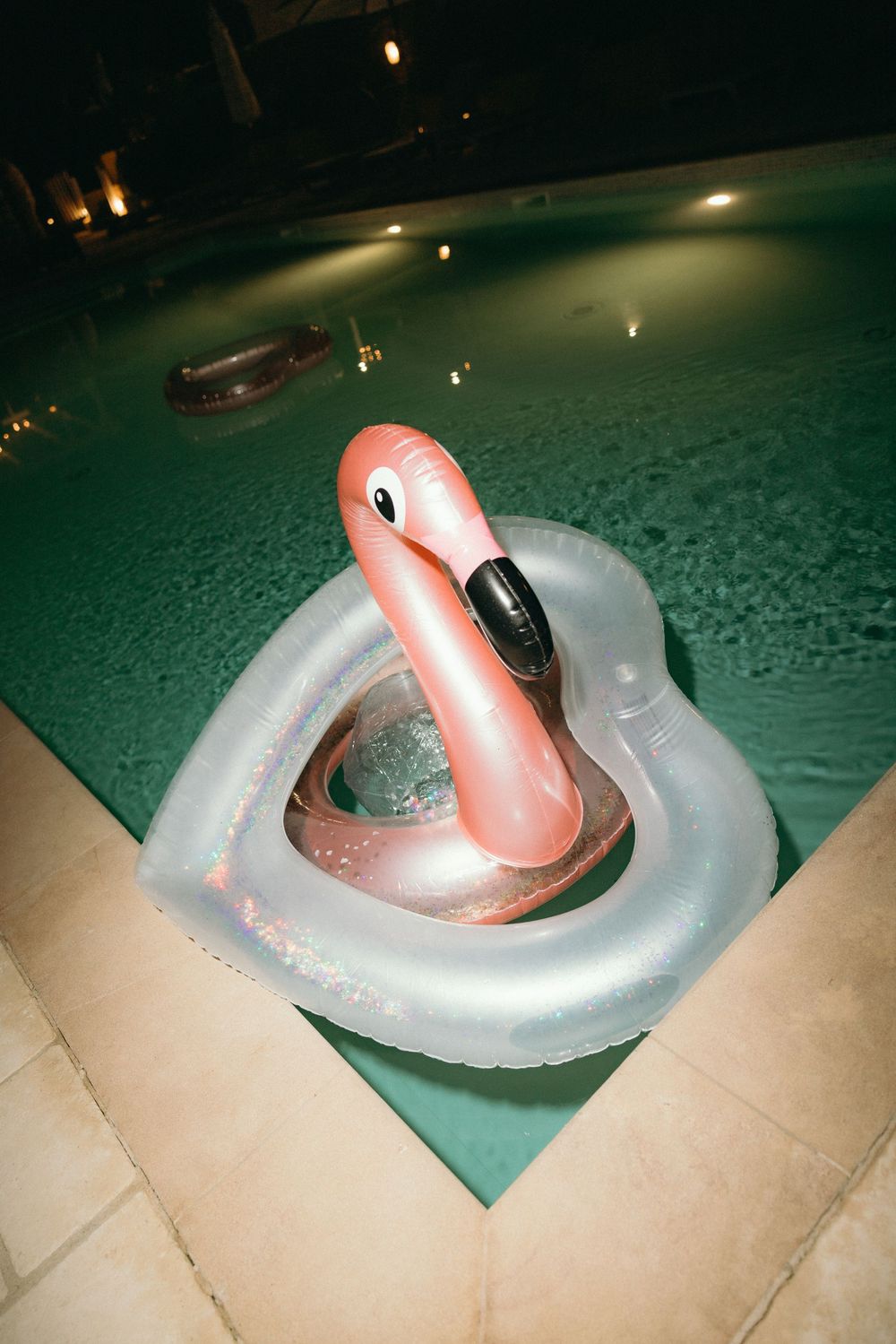 Pink pool float in turquoise water at night with ambient lighting.