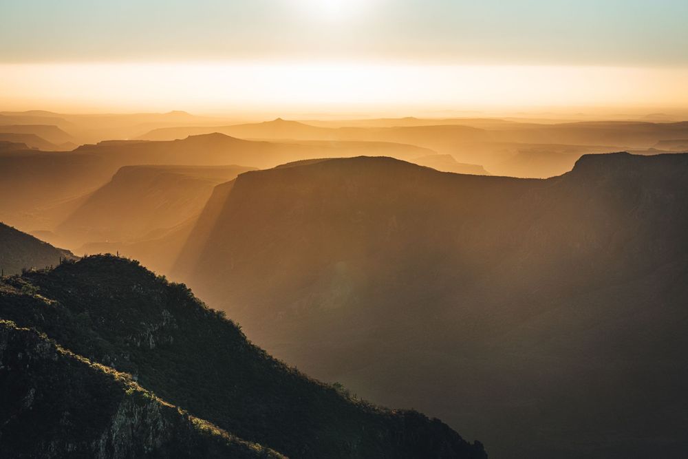 Golden sunlight illuminates layered mountain ridges creating a misty scenic landscape at sunset.