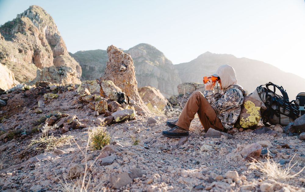 A person relaxes against rocky terrain in a mountainous landscape during golden hour.