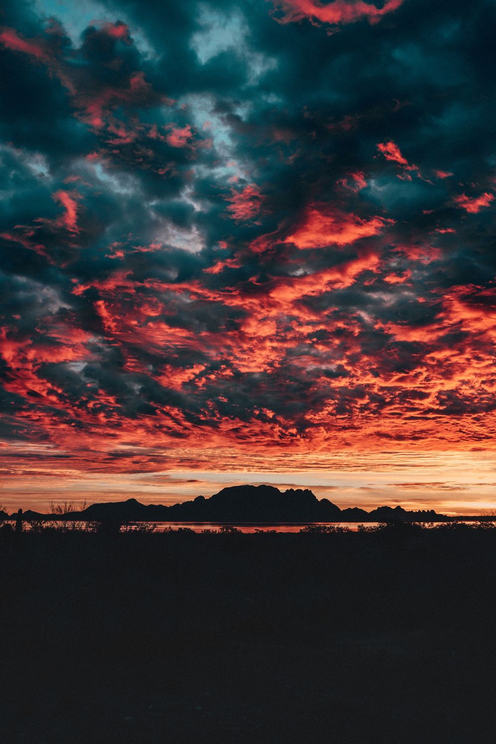 Dramatic sunset with fiery red clouds against a dark blue sky over a silhouetted landscape.