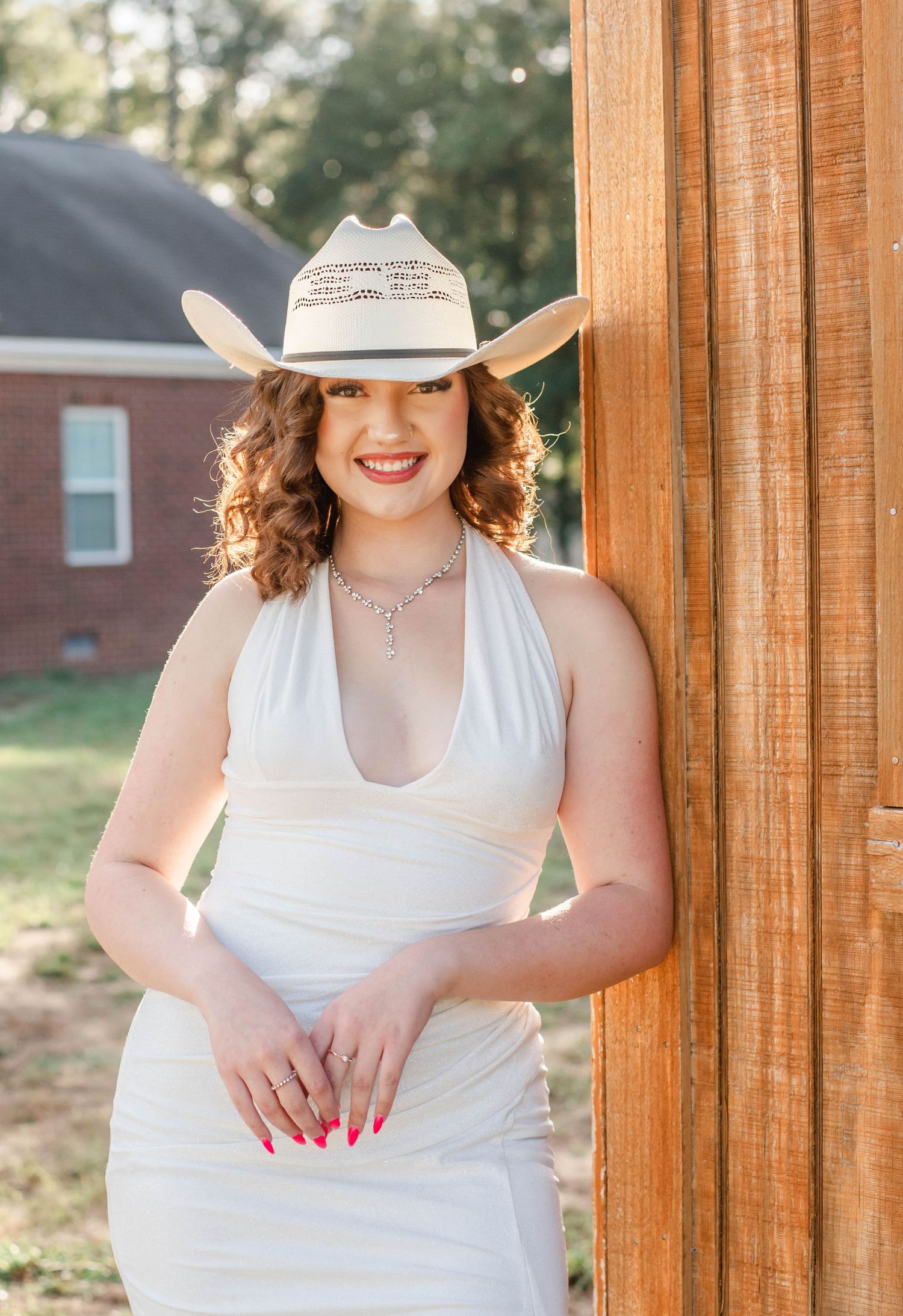 A person in a white sleeveless dress poses on a wooden porch with rustic columns in outdoor natural lighting.