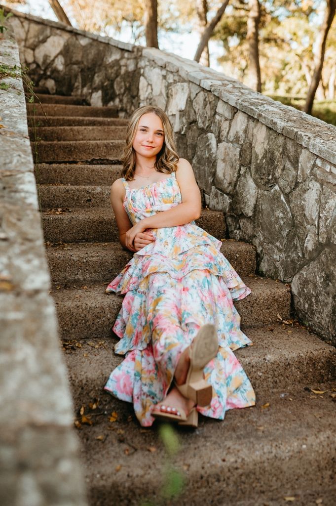 A floral dress flows gracefully on stone steps surrounded by natural outdoor scenery.