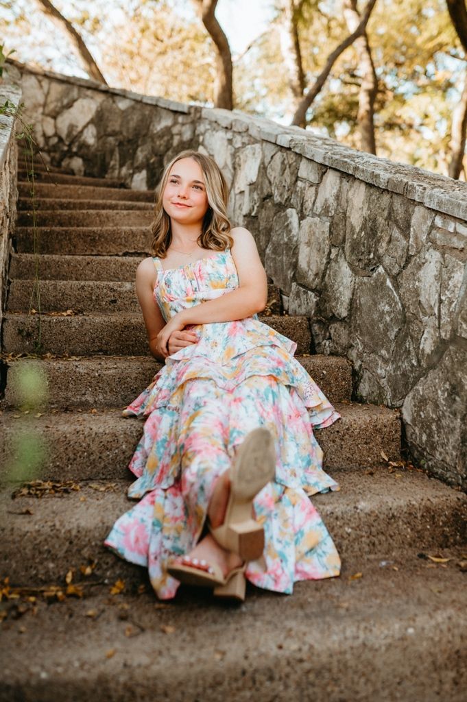 A whimsical photoshoot on stone steps showcasing a flowing floral dress with ruffled layers.