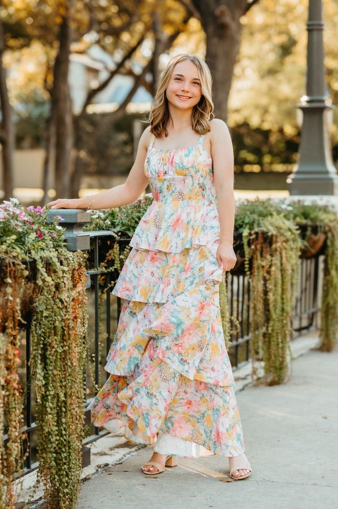 A collage of floral summer dresses photographed against a backdrop of trailing vines and greenery on a stone wall.