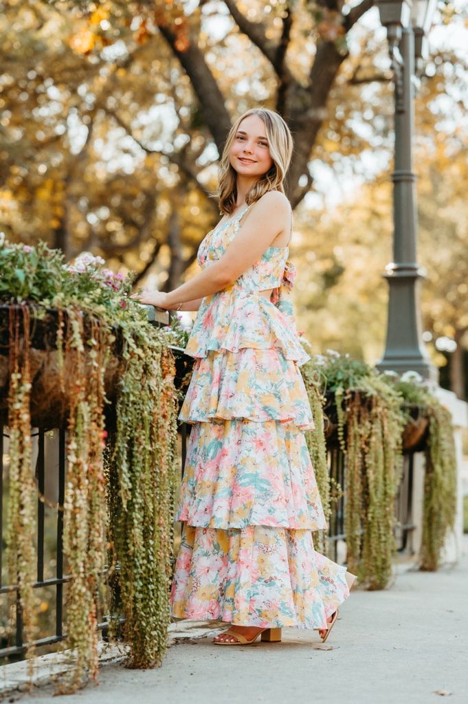 A floral sundress twirls against a backdrop of ivy-covered stone walls and autumn trees in golden light.