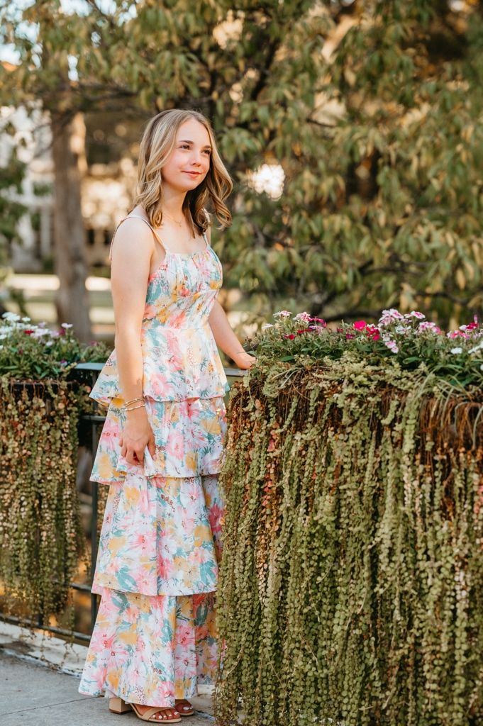 Floral tiered summer dress photographed in a garden setting with trailing vines and greenery.