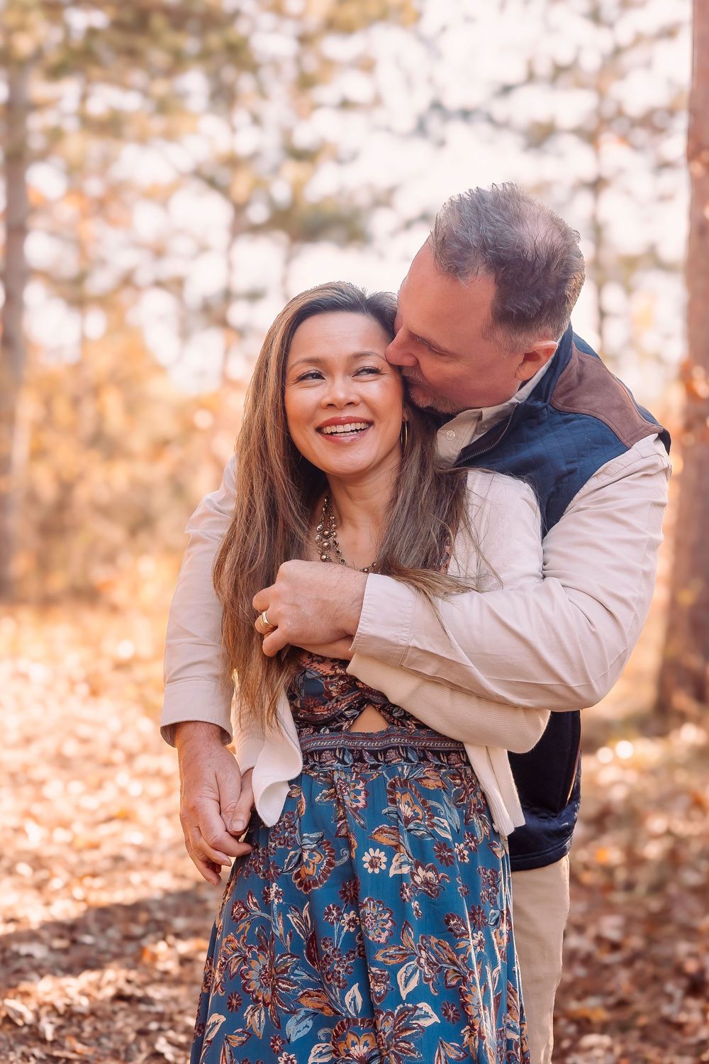 A romantic couple embraces in an autumn forest setting with golden sunlight filtering through trees.