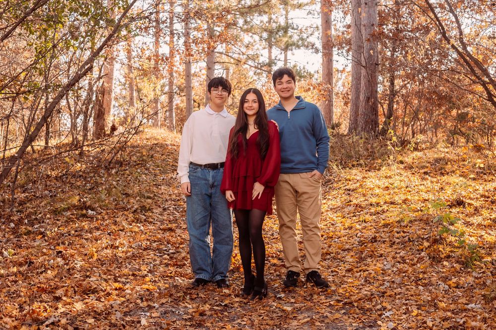 A group poses together on a wooded trail covered in fallen autumn leaves during a fall photo session.