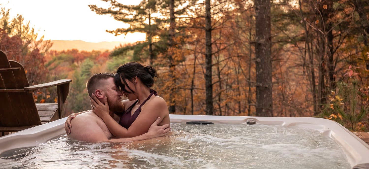 Romantic couple shares intimate moments in hot tub surrounded by autumn trees at sunset.