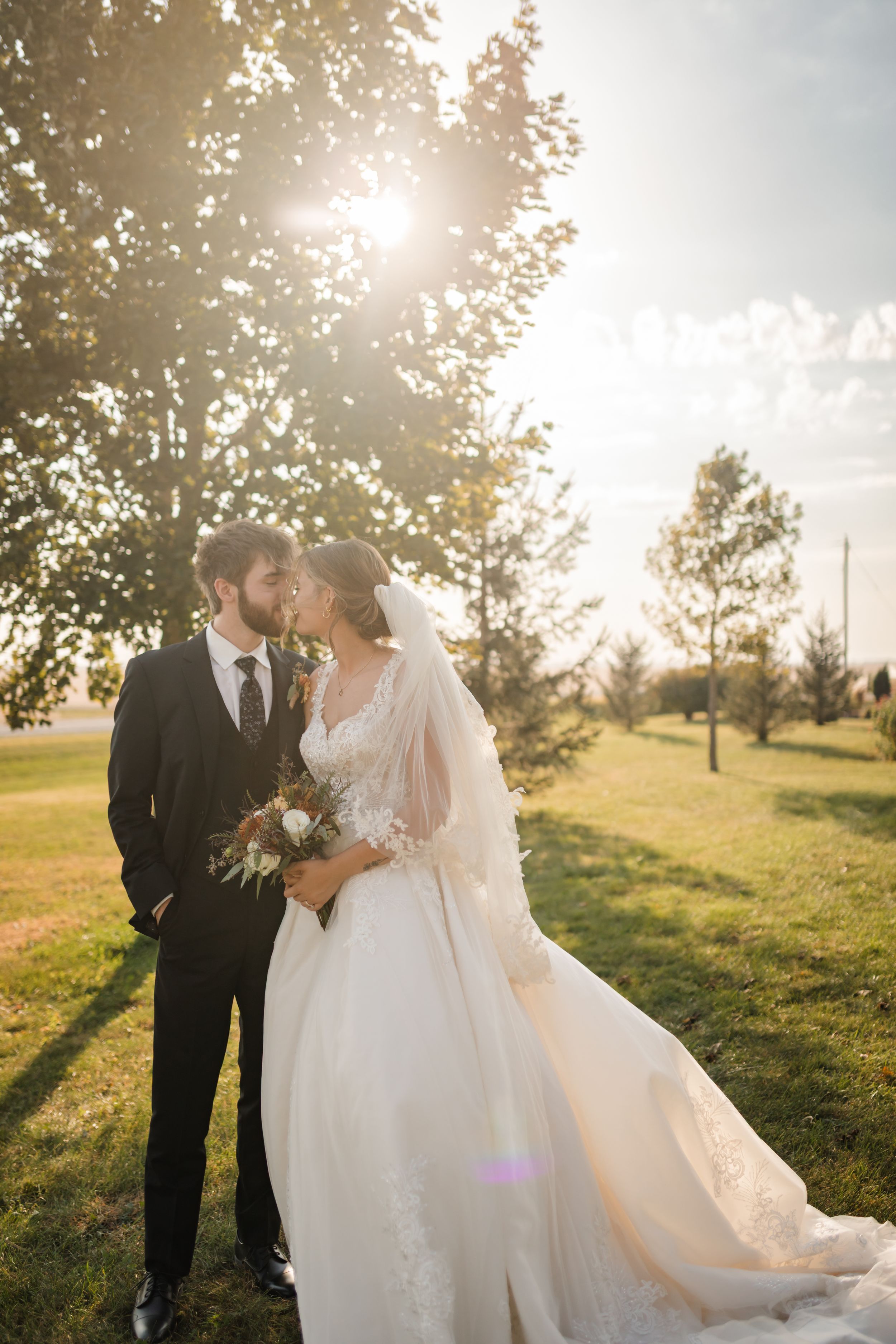 A romantic sunset wedding photo session with a couple embracing in a golden-lit field with trees in the background.