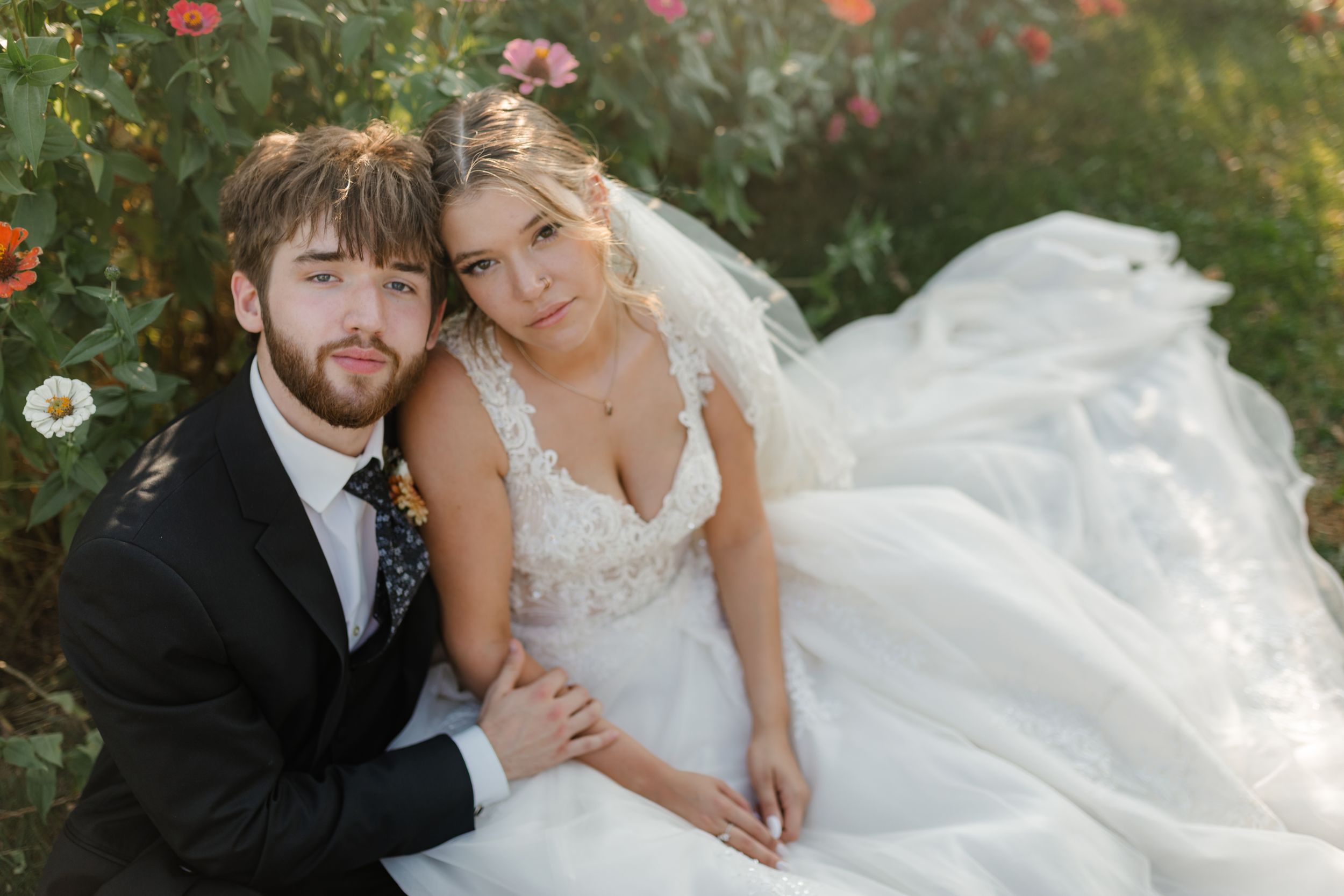 A wedding couple shares an intimate moment together in a garden setting with pink flowers in the background.