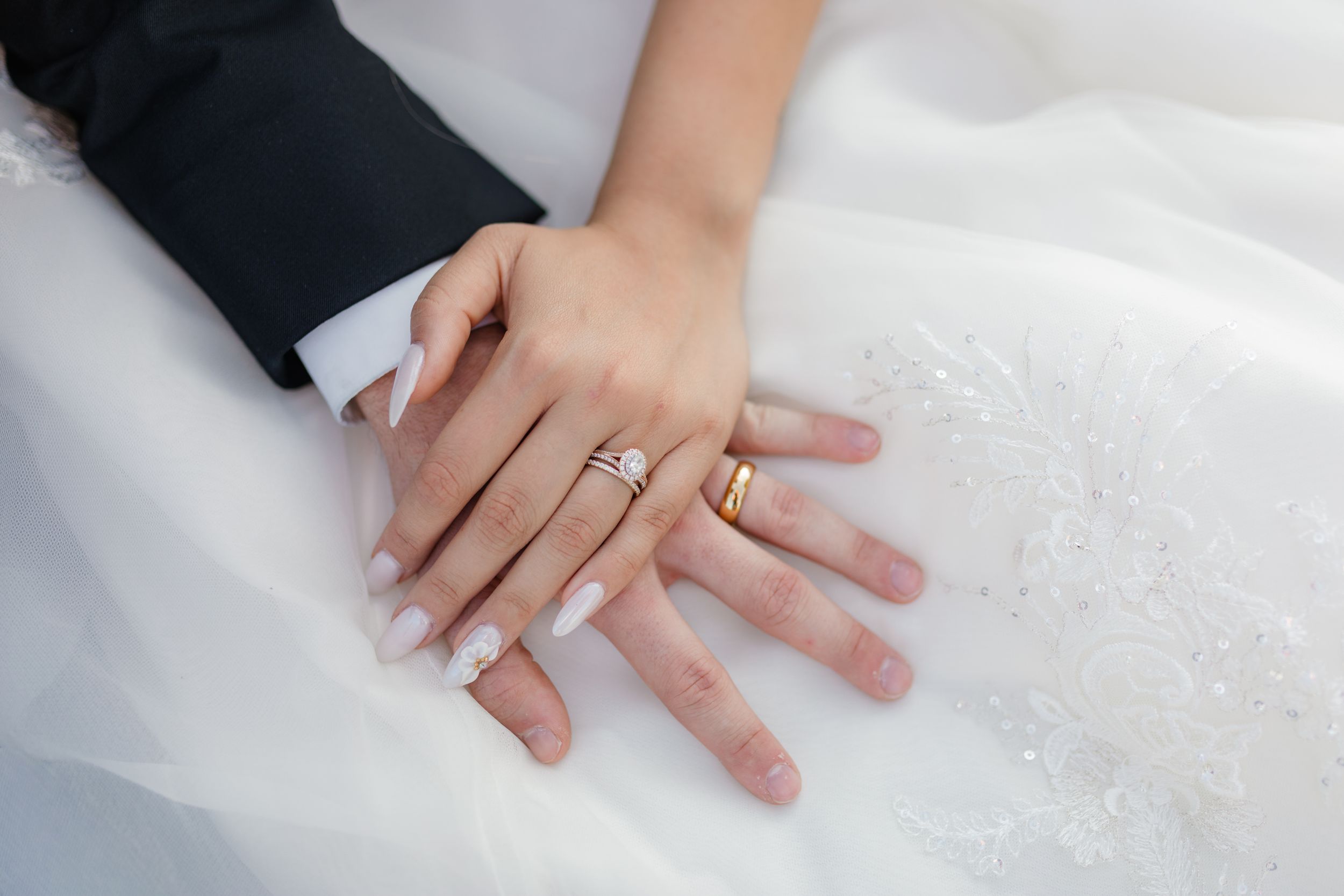 Close-up view of hands with engagement ring resting on white textured fabric.