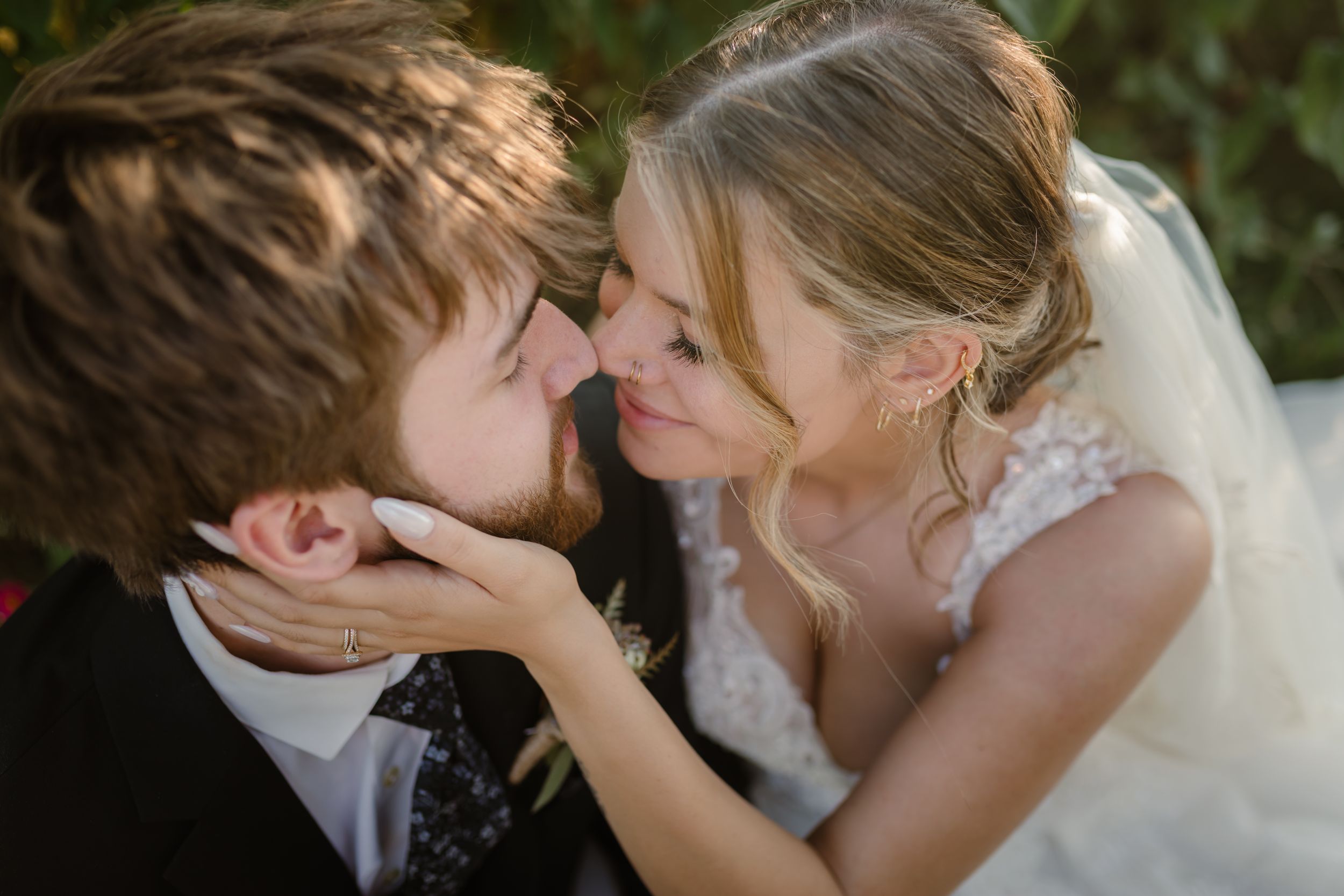 Romantic couple sharing a tender kiss during their wedding celebration outdoors.