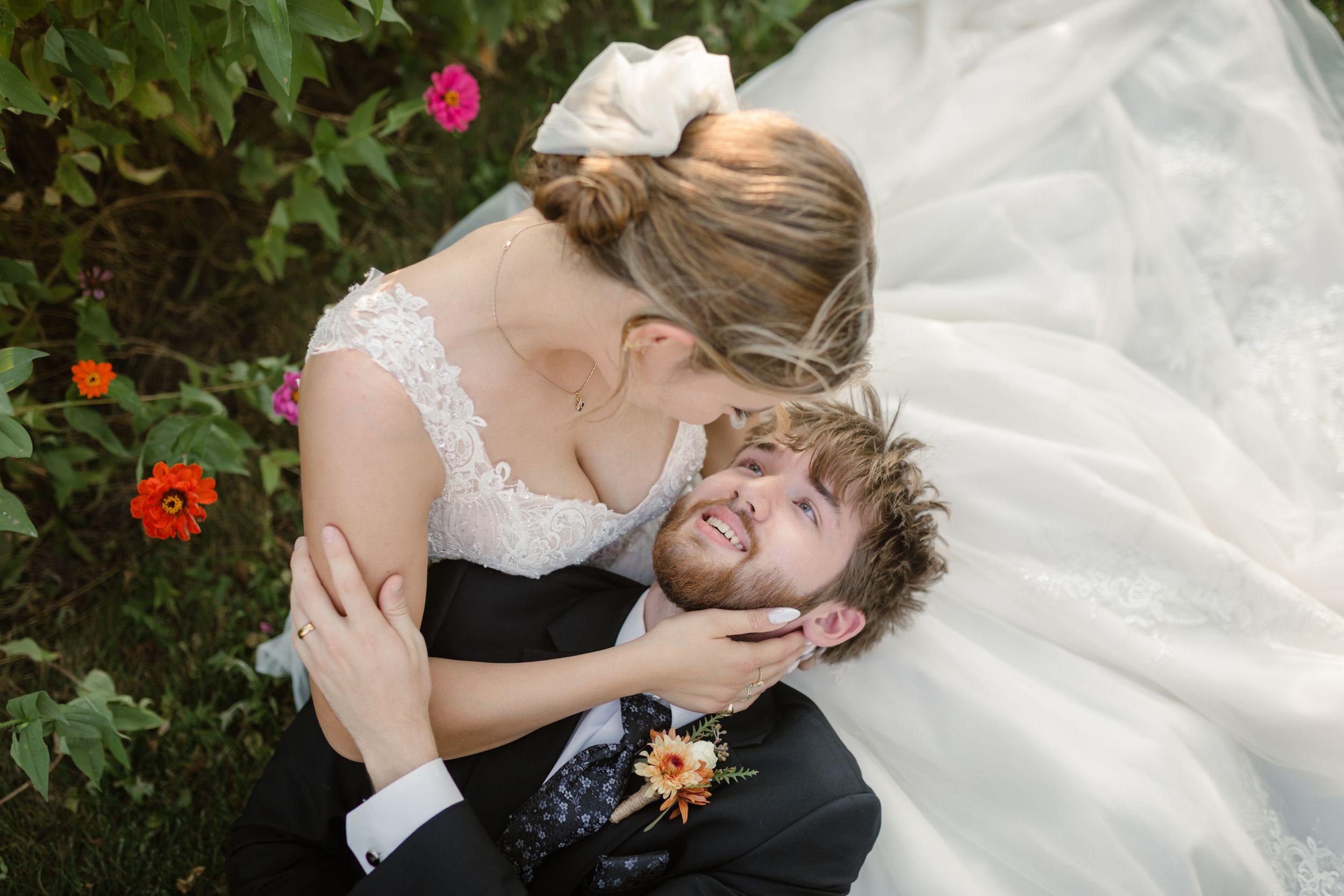A couple shares a tender moment in their wedding attire surrounded by blooming flowers in a garden.