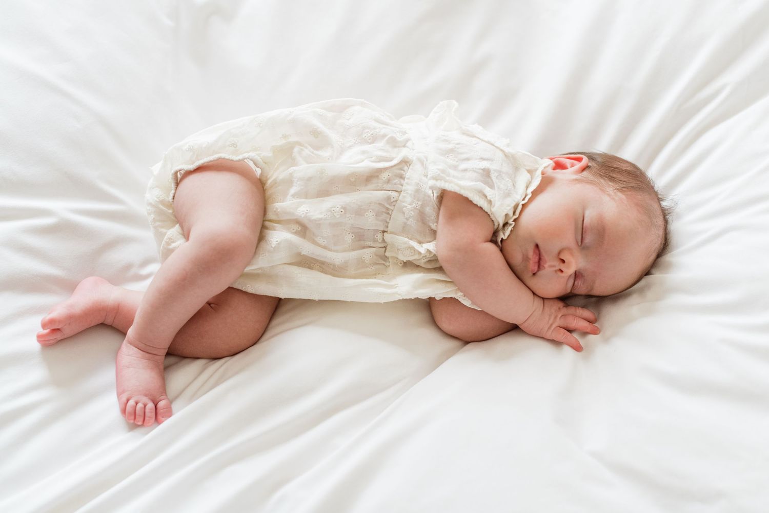 A sleeping baby lies peacefully on white bedding in a series of connected photos showing different angles and positions.