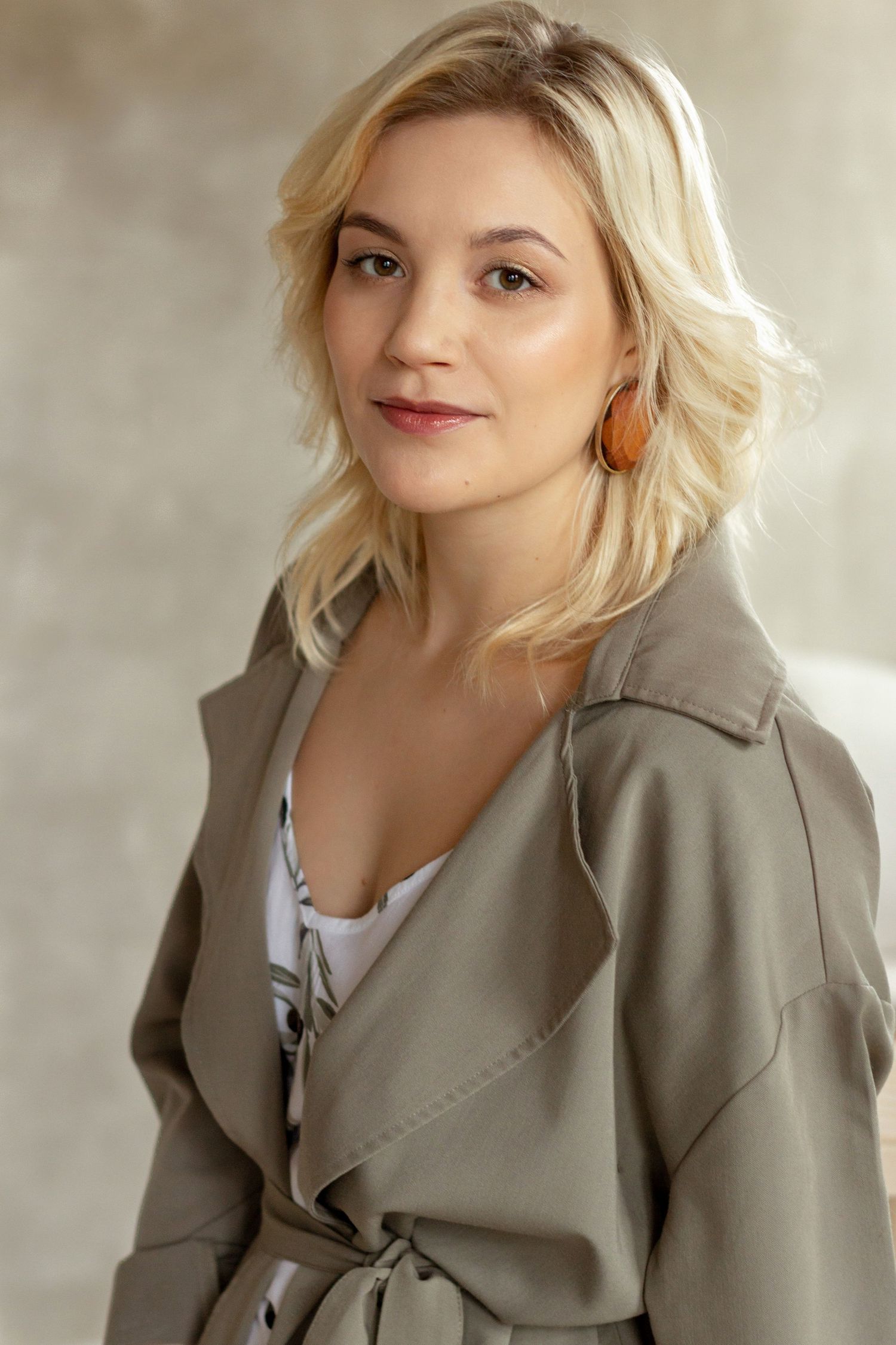 Professional headshot portrait with soft lighting showing blonde hair and taupe trench coat against neutral background, Cambridge, UK