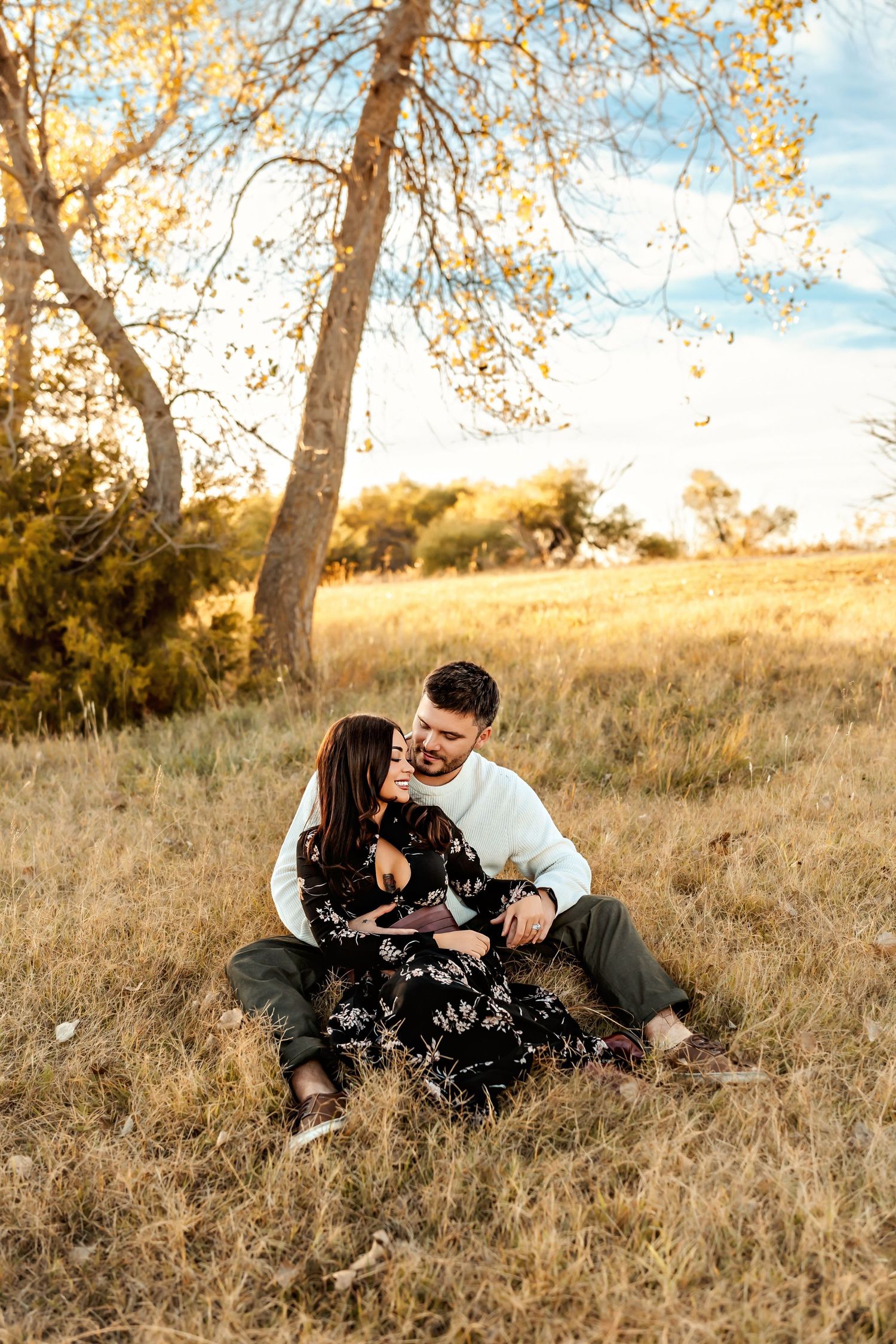 A couple shares a tender moment together while lying in a golden autumn field at sunset.