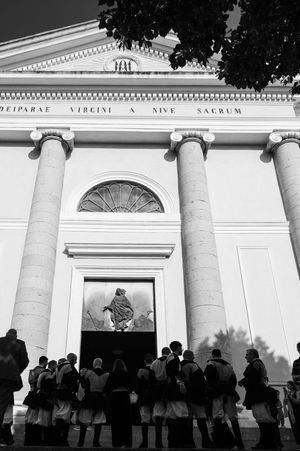 Classical white building facade with columns and gathering crowd silhouettes at sunset.
