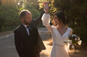 Wedding couple dances joyfully on a tree-lined path during sunset.