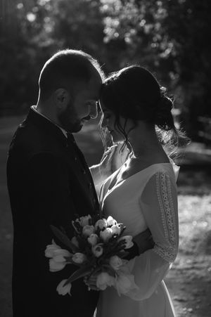 Black and white portrait captures tender moment between bride and groom with bouquet.