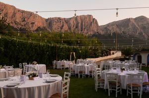 An outdoor wedding reception setup with string lights against dramatic red mountain cliffs at sunset.
