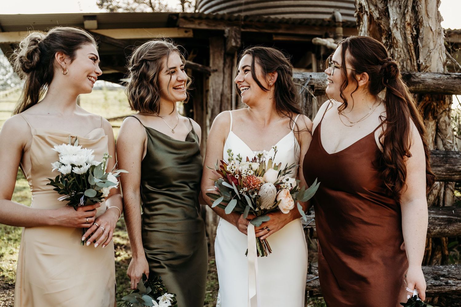 Bridal party in earth-toned dresses shares joyful moment at outdoor wedding venue.
