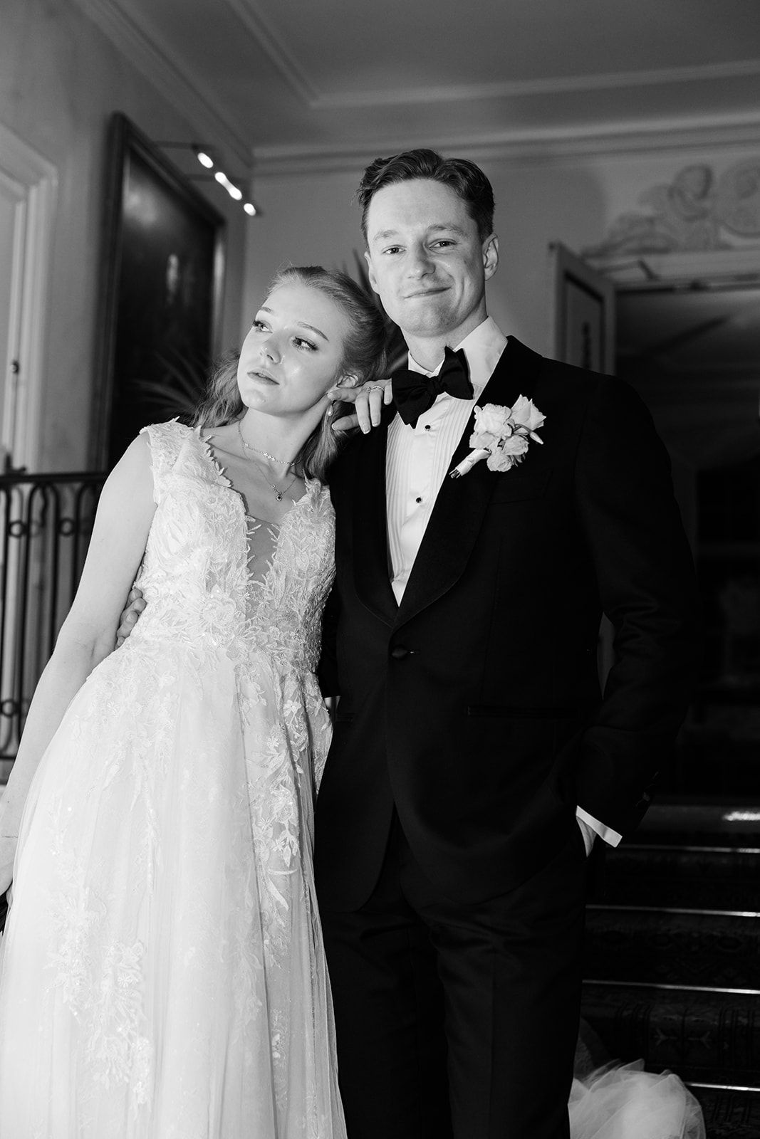 A black and white wedding photograph showing a couple in formal attire standing together in an elegant indoor setting.