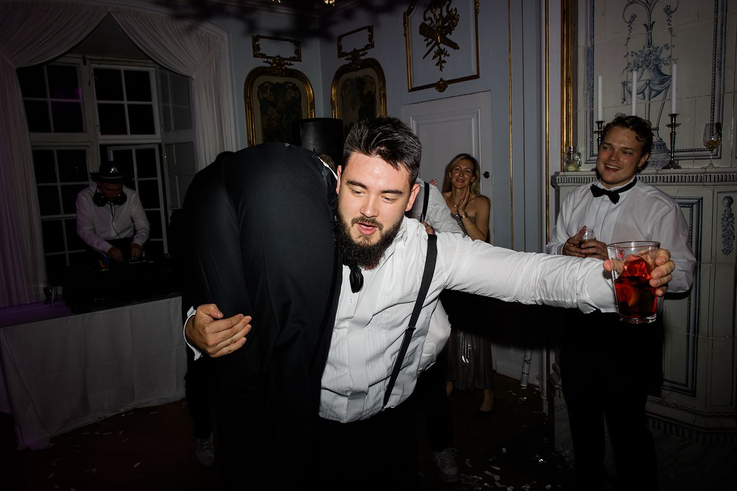 Wedding guests dancing and celebrating on a dance floor under purple lighting at a reception party.