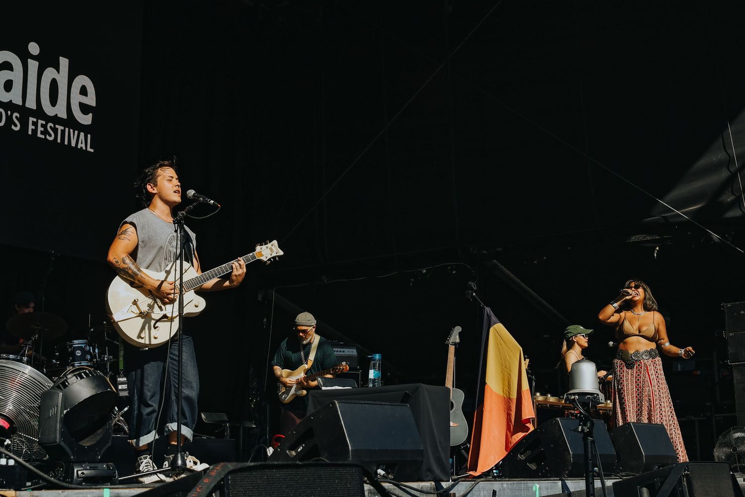 Musicians performing on stage at WOMADelaide festival with Aboriginal flag displayed prominently.