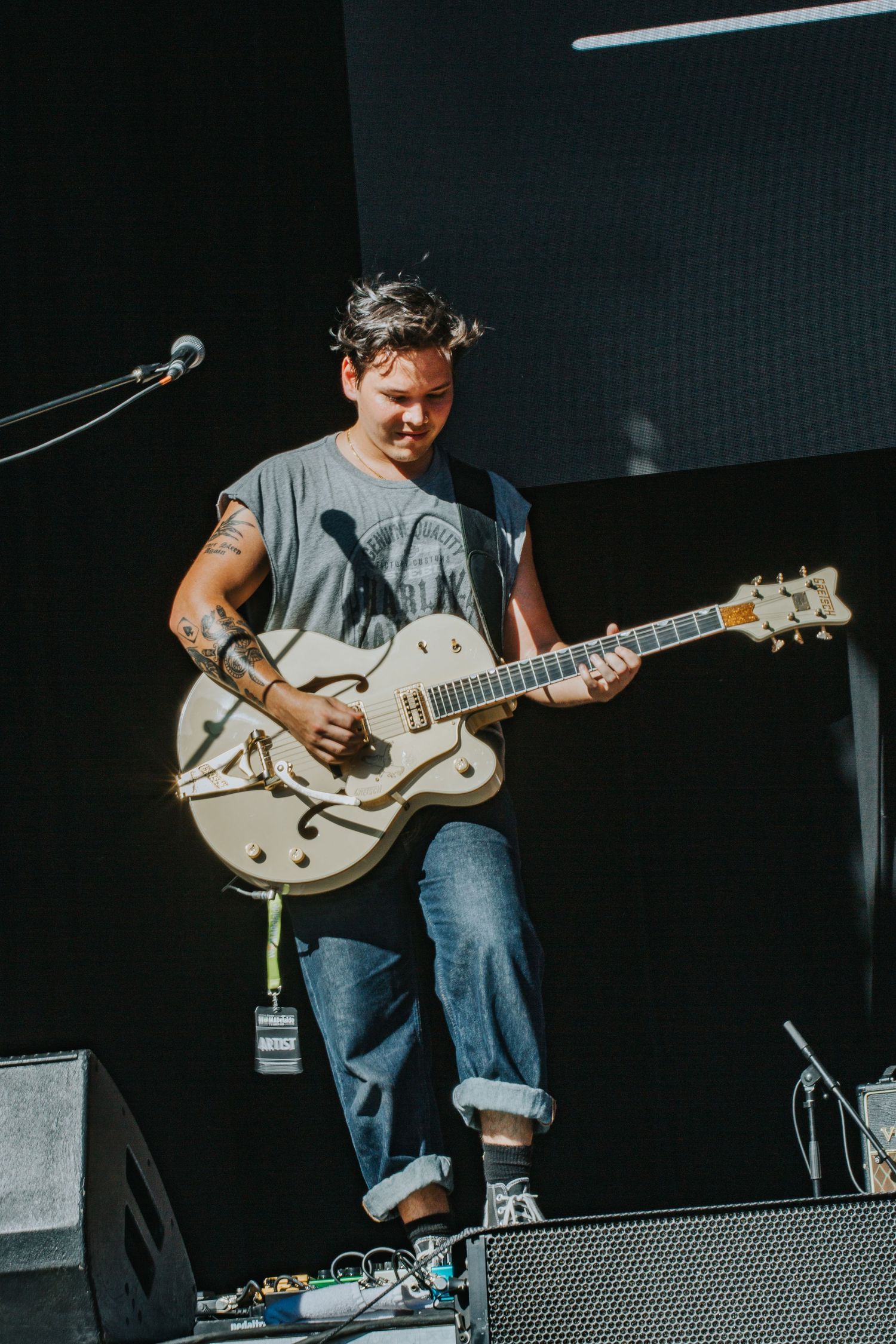 Young male guitarist smiling while playing white Gretsch hollow body guitar on outdoor festival stage.