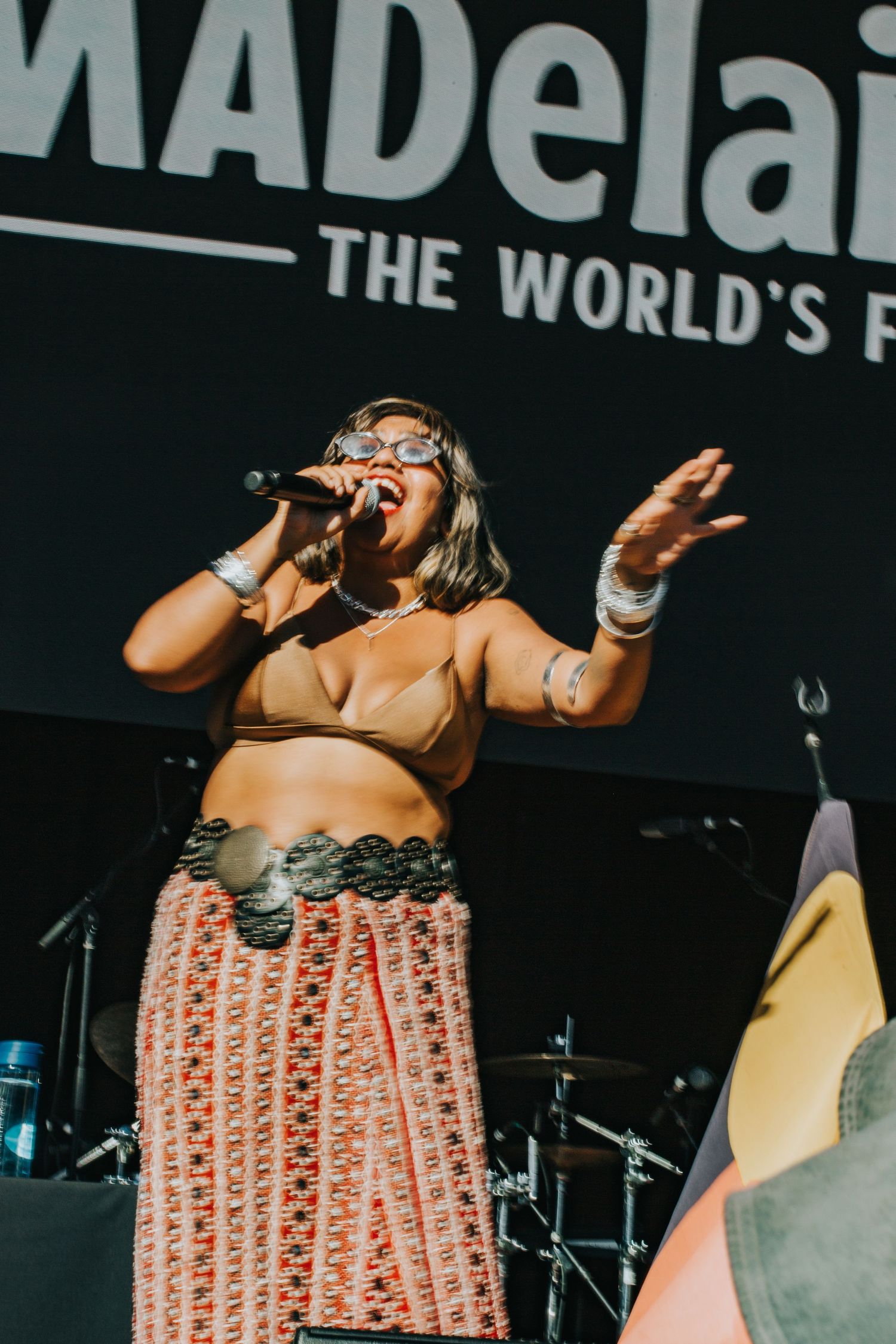 Female vocalist singing passionately on stage at WOMADelaide wearing traditional patterned skirt.